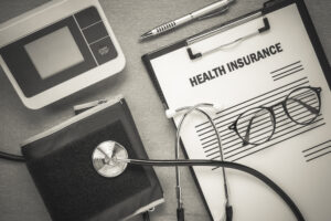 Top view health insurance form eyeglasses and pulse gauge with stethoscope on wooden background.