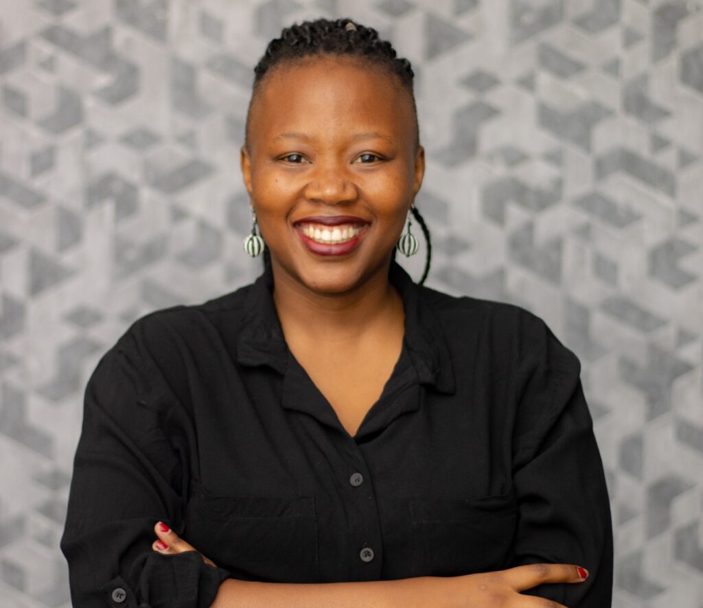Larona Lekgobe, A black woman smiling while folding her arms. She is wearing a black shirt.